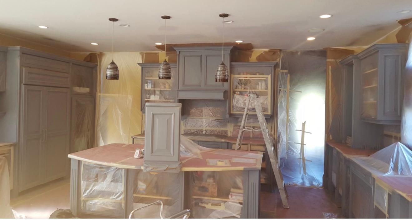 Kitchen under renovation with cabinets, countertops, and plastic-covered surfaces, viewed from the center of the room