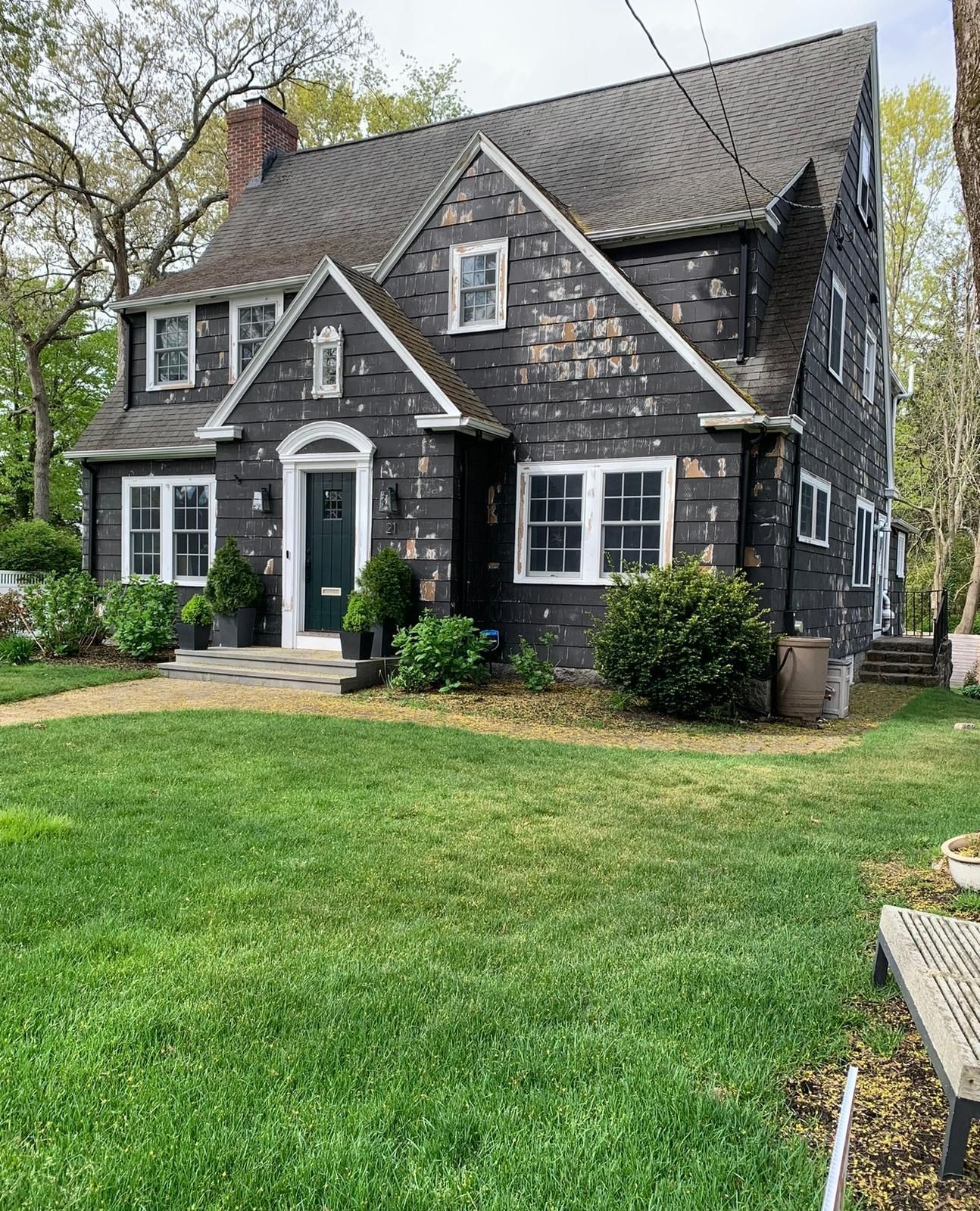 Dark gray house with white trim, steep gabled roof, and a large green lawn in front