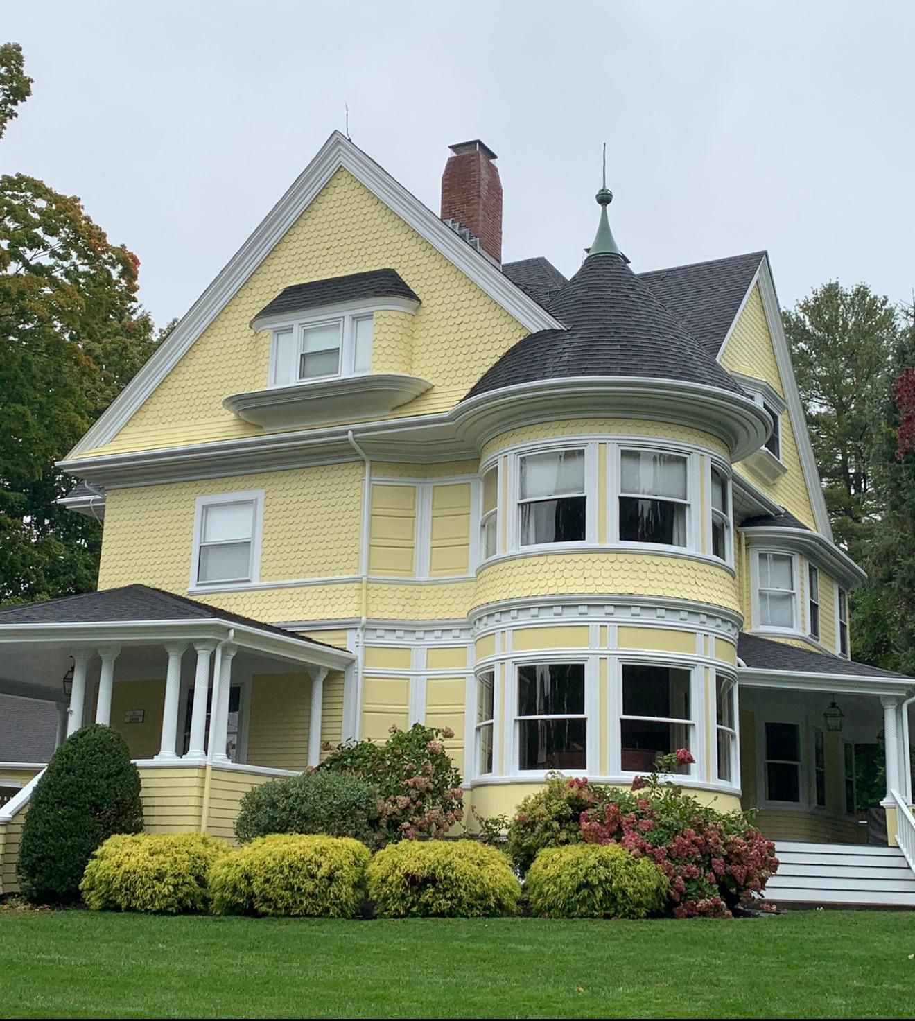 Yellow Victorian-style house with a turret, white trim, and a green lawn