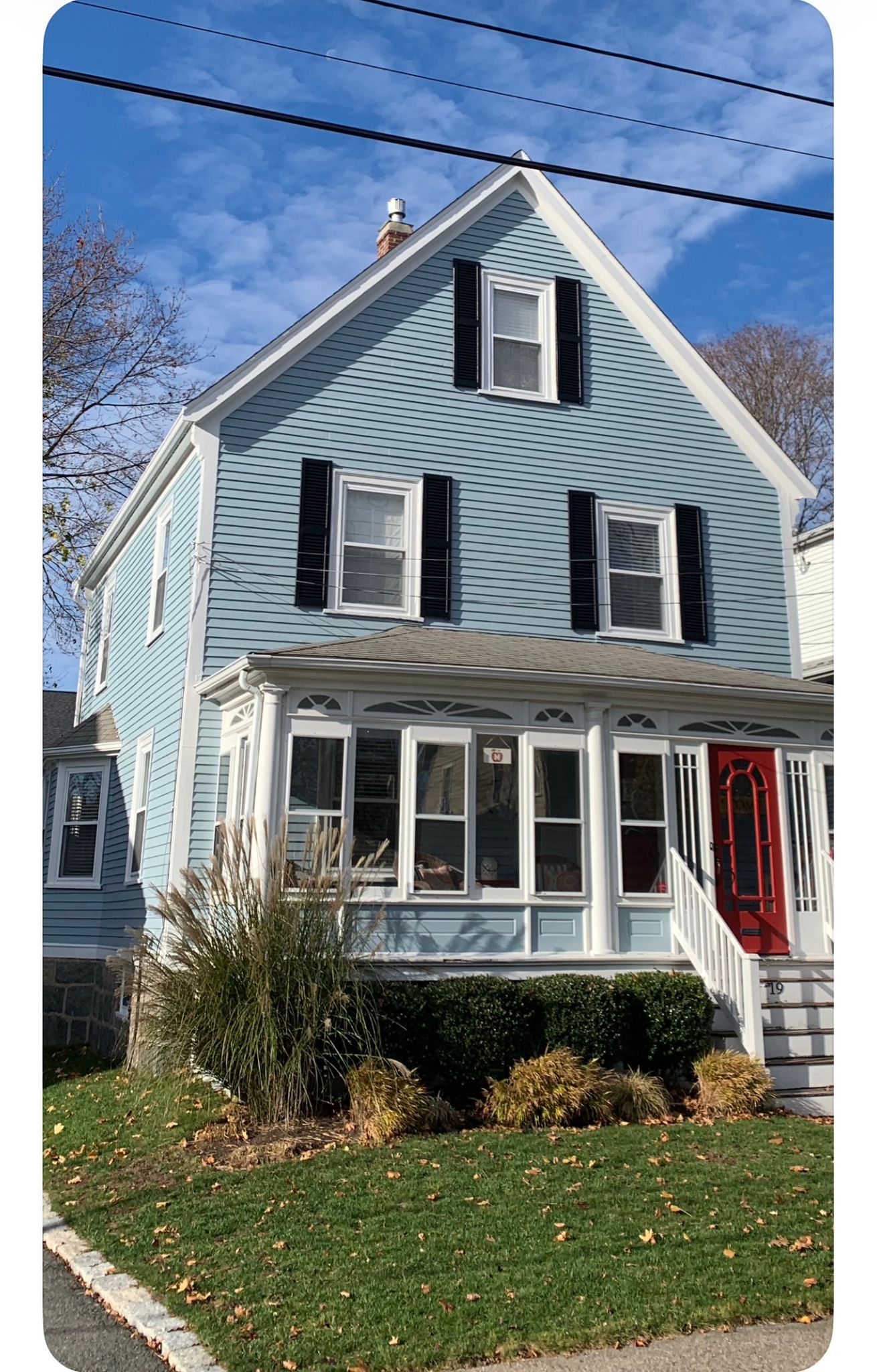 Blue two-story house with white trim and screened porch, a red front door, and a grassy yard under a clear sky