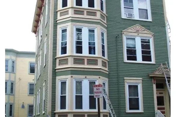 Victorian-style apartment building with green and beige siding and a no parking sign by the entrance