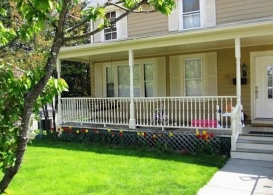 Yellow house with white porch railing, green lawn, and trees in front