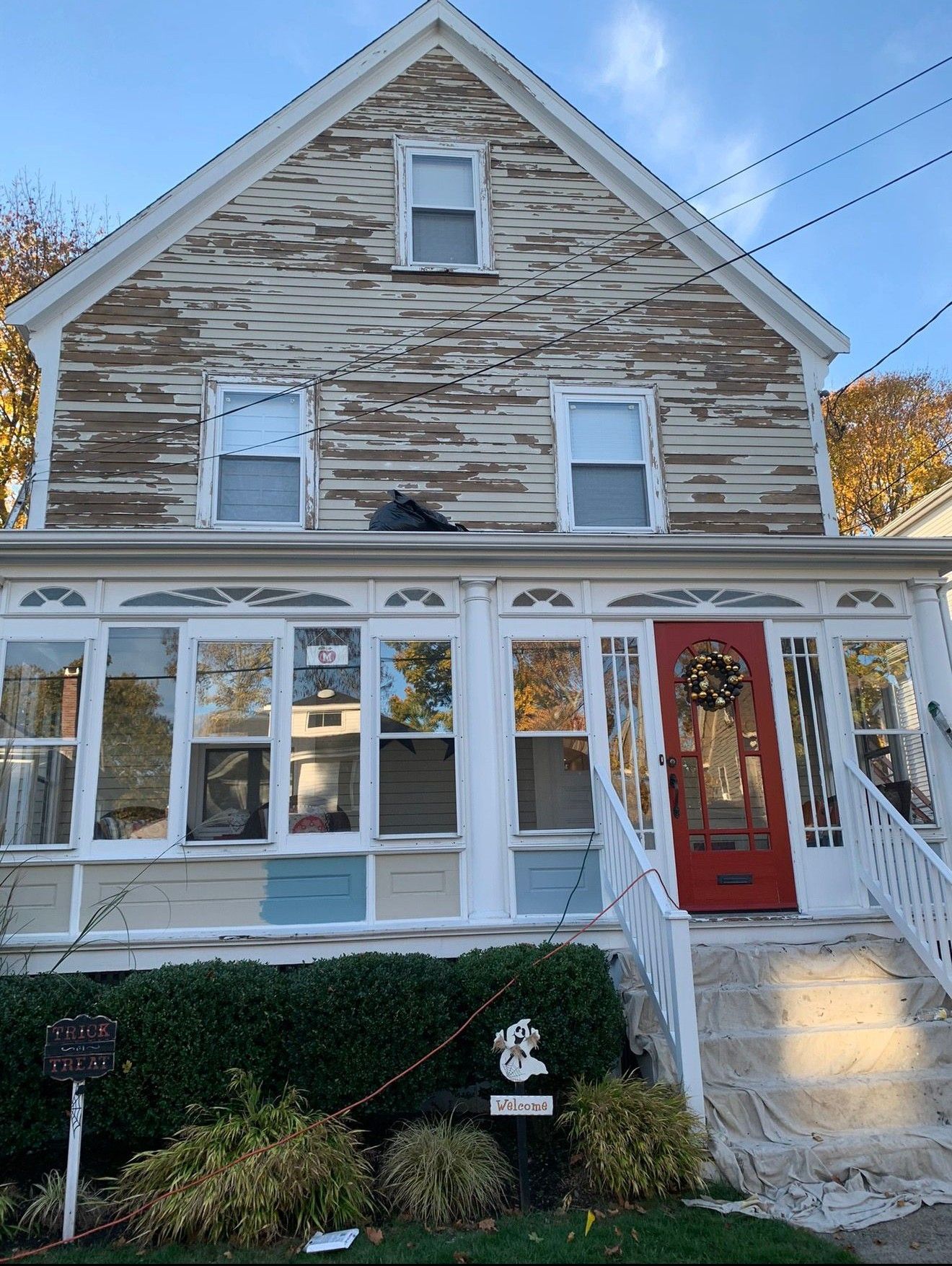 Two-story house with white porch, stone siding, and a red front door in autumn light