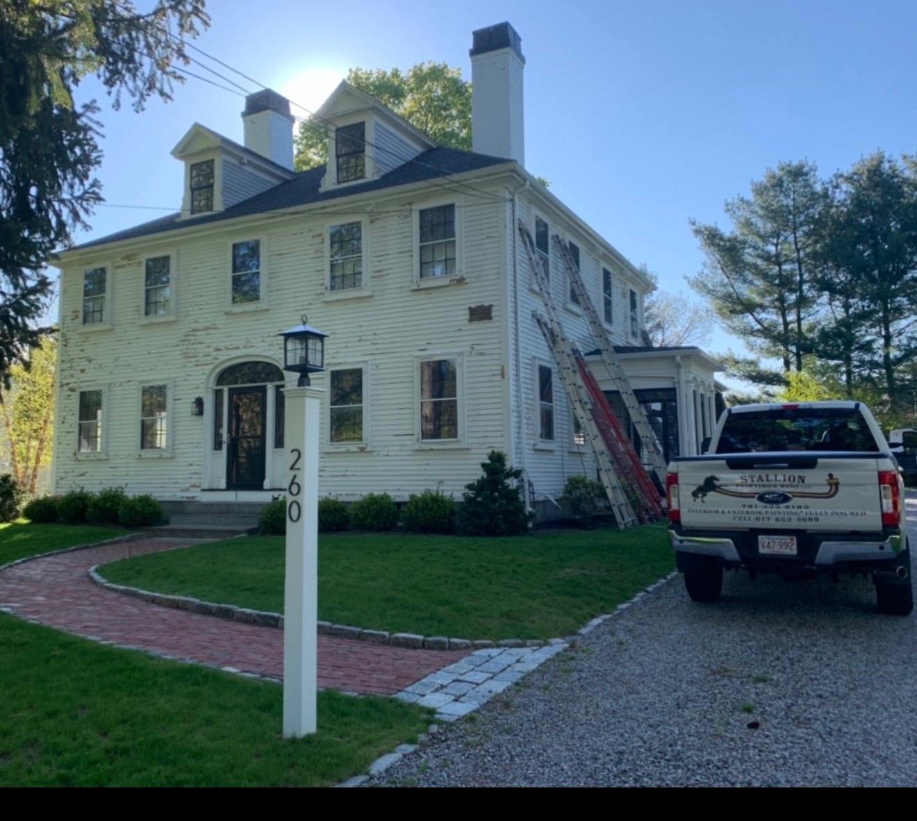 Historic white house with laddered roof, gravel driveway, and a white SUV parked beside it