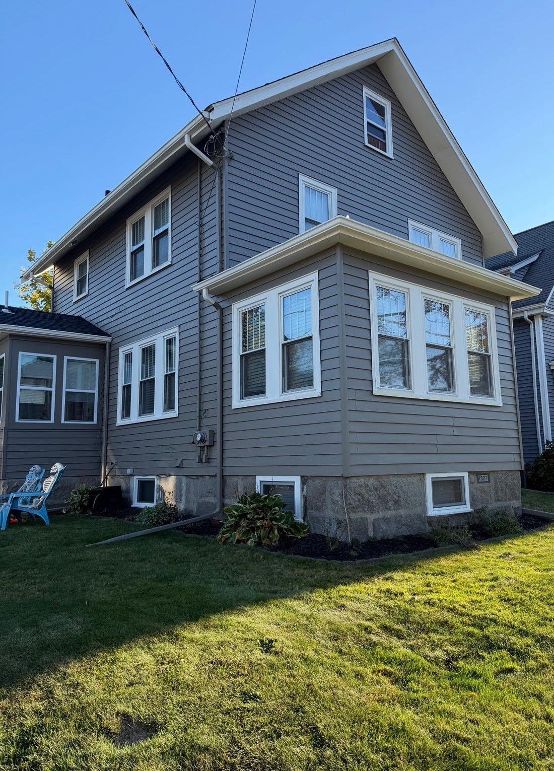 Gray two-story house with white trim and sunlit lawn under a blue sky
