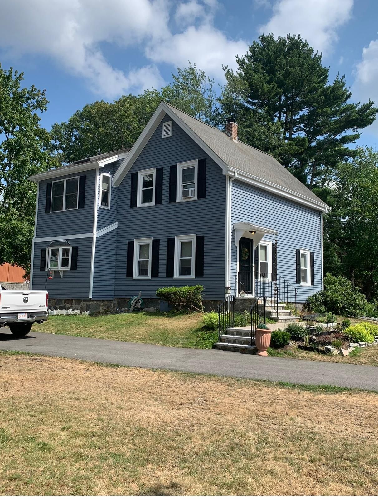 Blue two-story house with white trim and a steep roof, surrounded by trees and a front yard