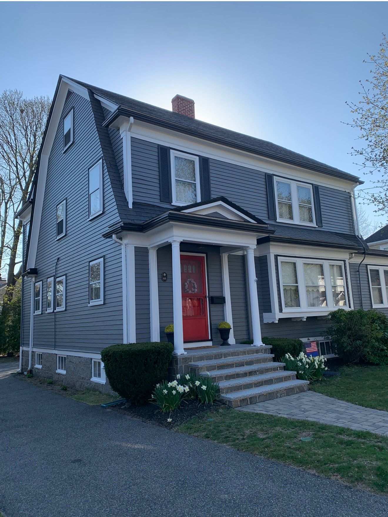 Gray two-story house with white trim, a red front door, porch, and front steps beside a gravel driveway.