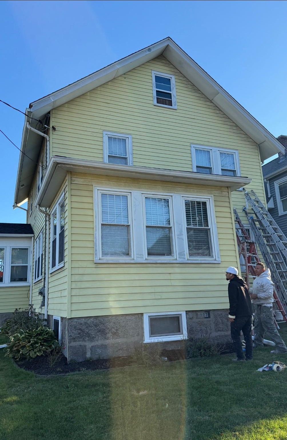Yellow house exterior with two people standing by an outdoor staircase under a blue sky