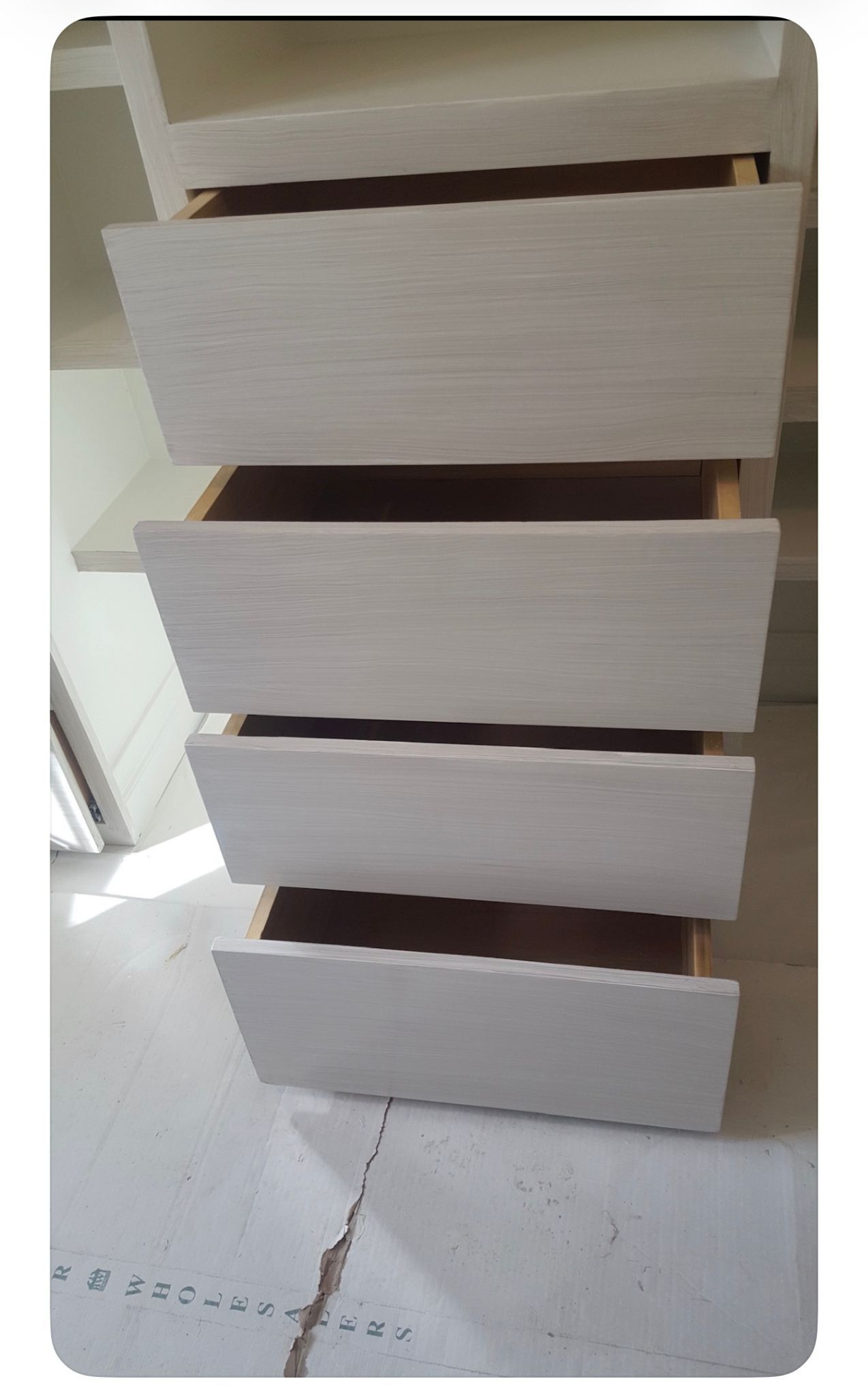 Stack of four white wooden drawers or boxes, slightly misaligned, on a light floor.
