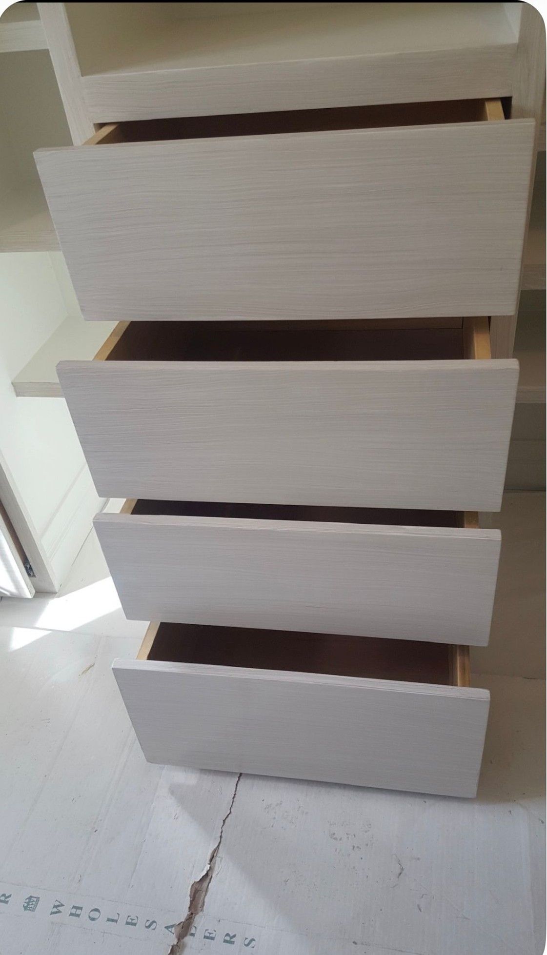 Stacked white drawer fronts on a light-colored cabinet in a room.
