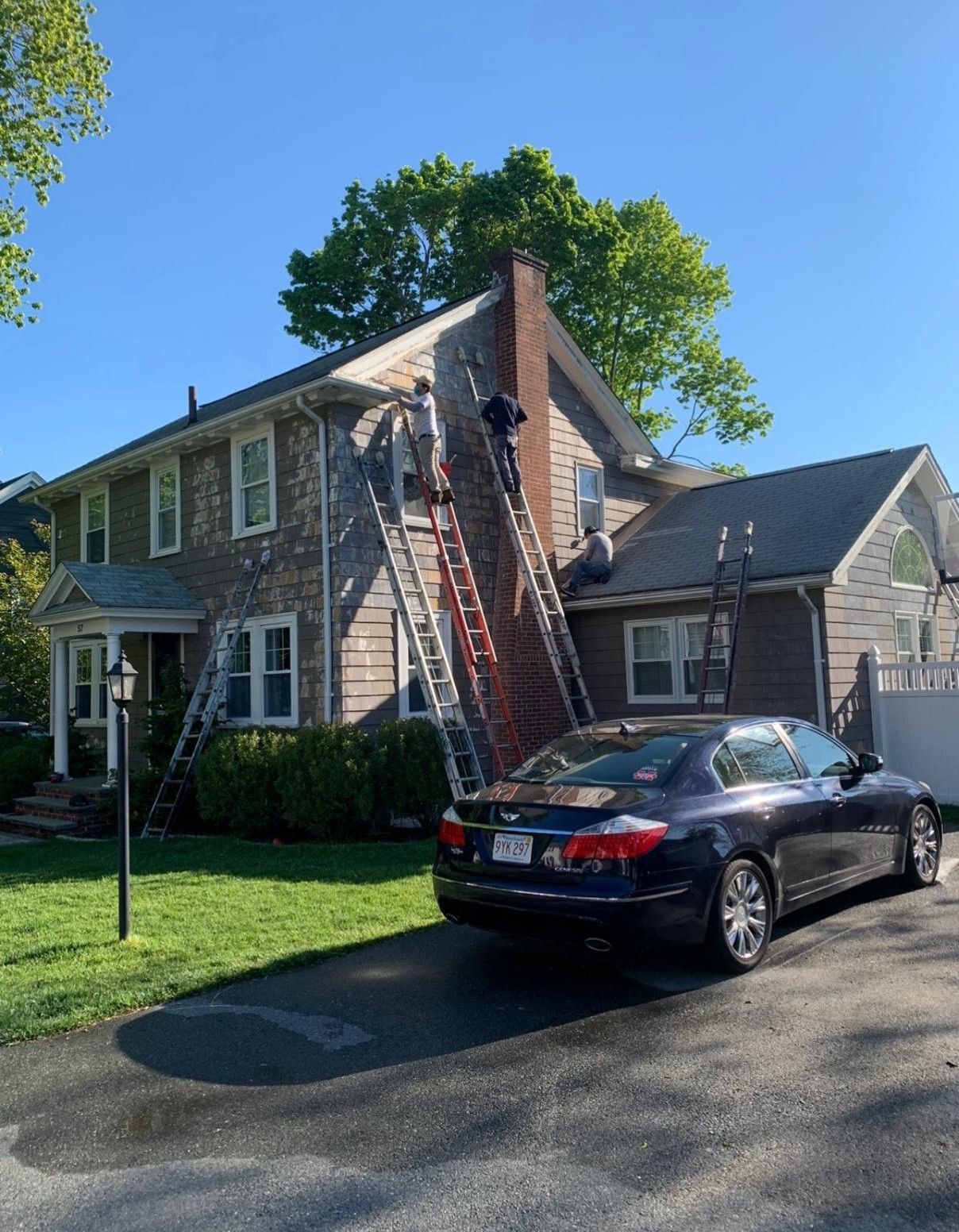 Two-story house with a ladder on the roof and a black sedan parked in the driveway