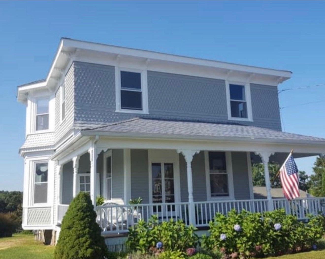 Gray two-story house with white trim, porch, and American flag on a sunny day