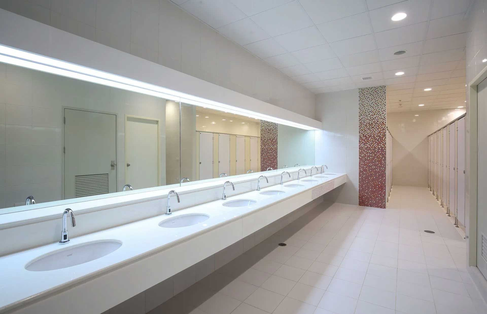 White public restroom with a long countertop with sinks and mirrors, stalls on the right.