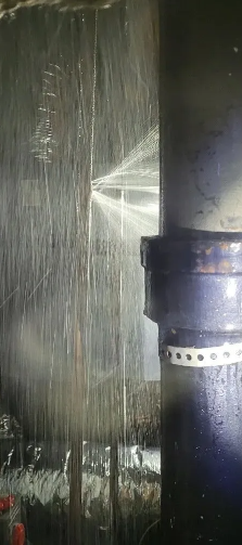 Water spraying out of a pipe, likely from a leak, with close-up of a black pipe and connecting joint.
