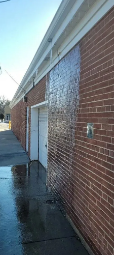 A brick building with wet walls and sidewalk, a garage door, and a bright sky.