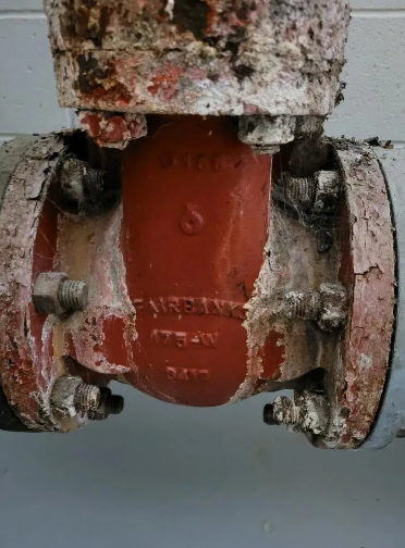 Red and white industrial valve with bolts and partially flaked paint.