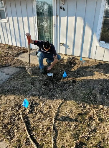 Person using a shovel and working on a ground near a house. Blue markers are also visible.