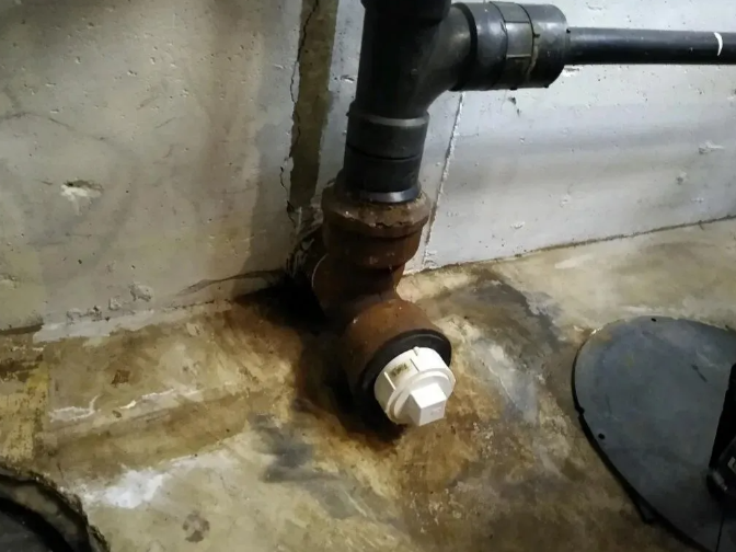 Brown and black pipes connected to a white capped pipe on a concrete floor with water stains.