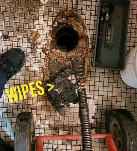 Toilet drain clogged with wipes, snake tool in use on tiled floor.