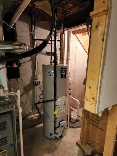 A gas water heater in a basement with pipes, and ductwork. Adjacent to a wooden structure.