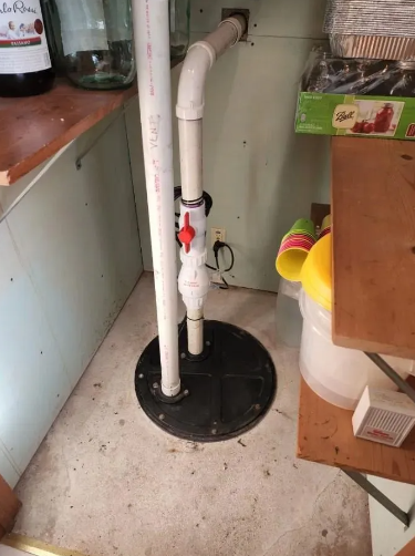 Sump pump system with white PVC pipes, red valve, and black basin on a concrete floor.