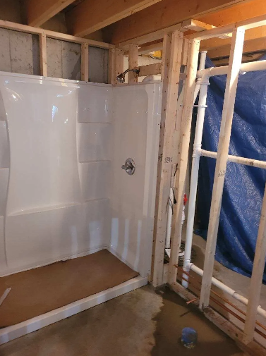 White shower stall framed in wood in a basement under construction.