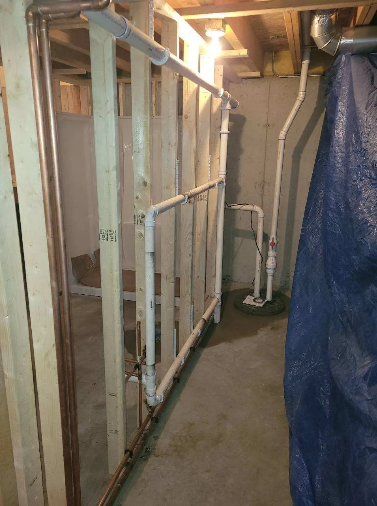 Basement with exposed plumbing and wooden framing. Copper pipes and white PVC pipes run along the wall.