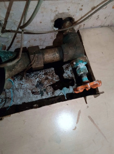 Water pipes with corrosion and a shut-off valve within a cutout in a wall.