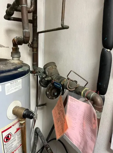 Water heater and associated copper pipes and valves. An orange tag hangs in front of the valve.