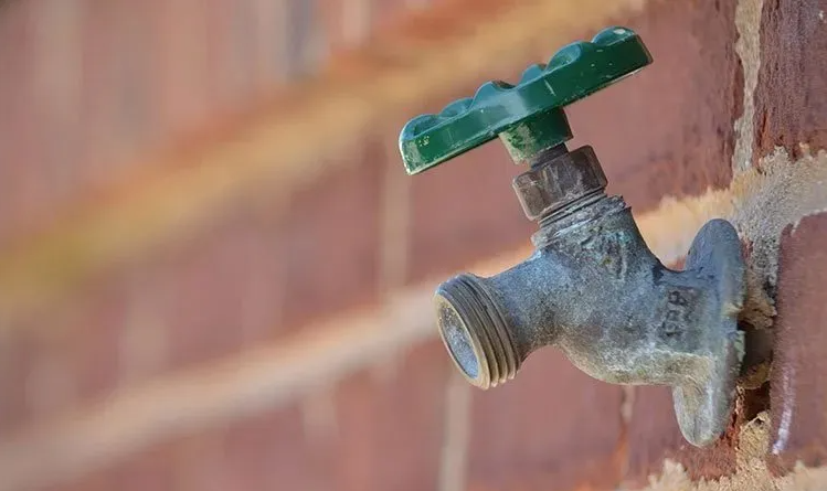 Green-handled water spigot on a brick wall.