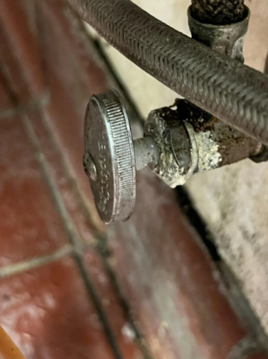 Metal water shut-off valve with white mineral buildup near a tiled wall and braided hose.