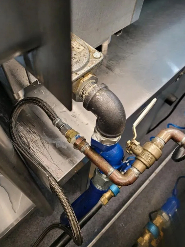 Plumbing with copper pipe, black elbow fitting, and flexible hose attached to a metal surface.