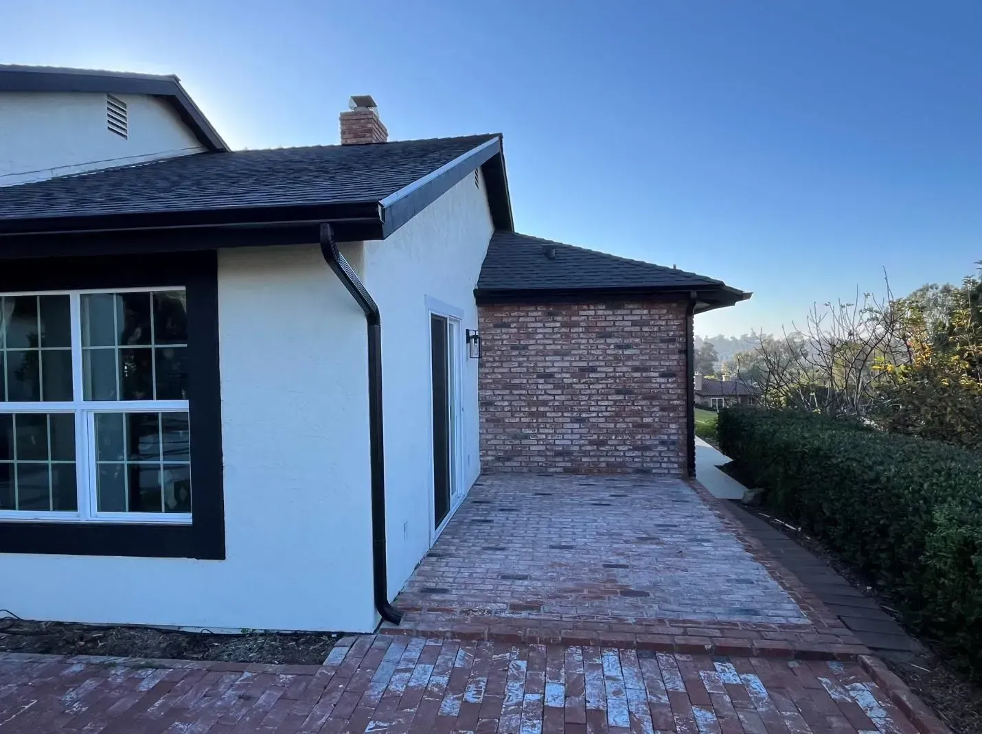 Exterior of a house with white stucco and black trim, brick patio, and brick wall.