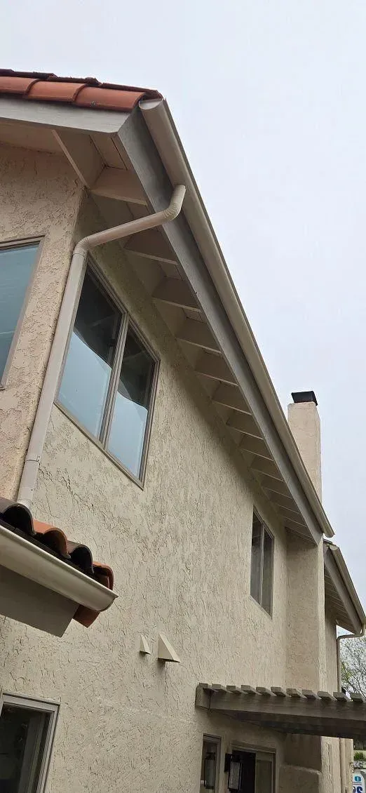 A house exterior with stucco walls, windows, and a chimney under an overcast sky.  The house has a gutter system.