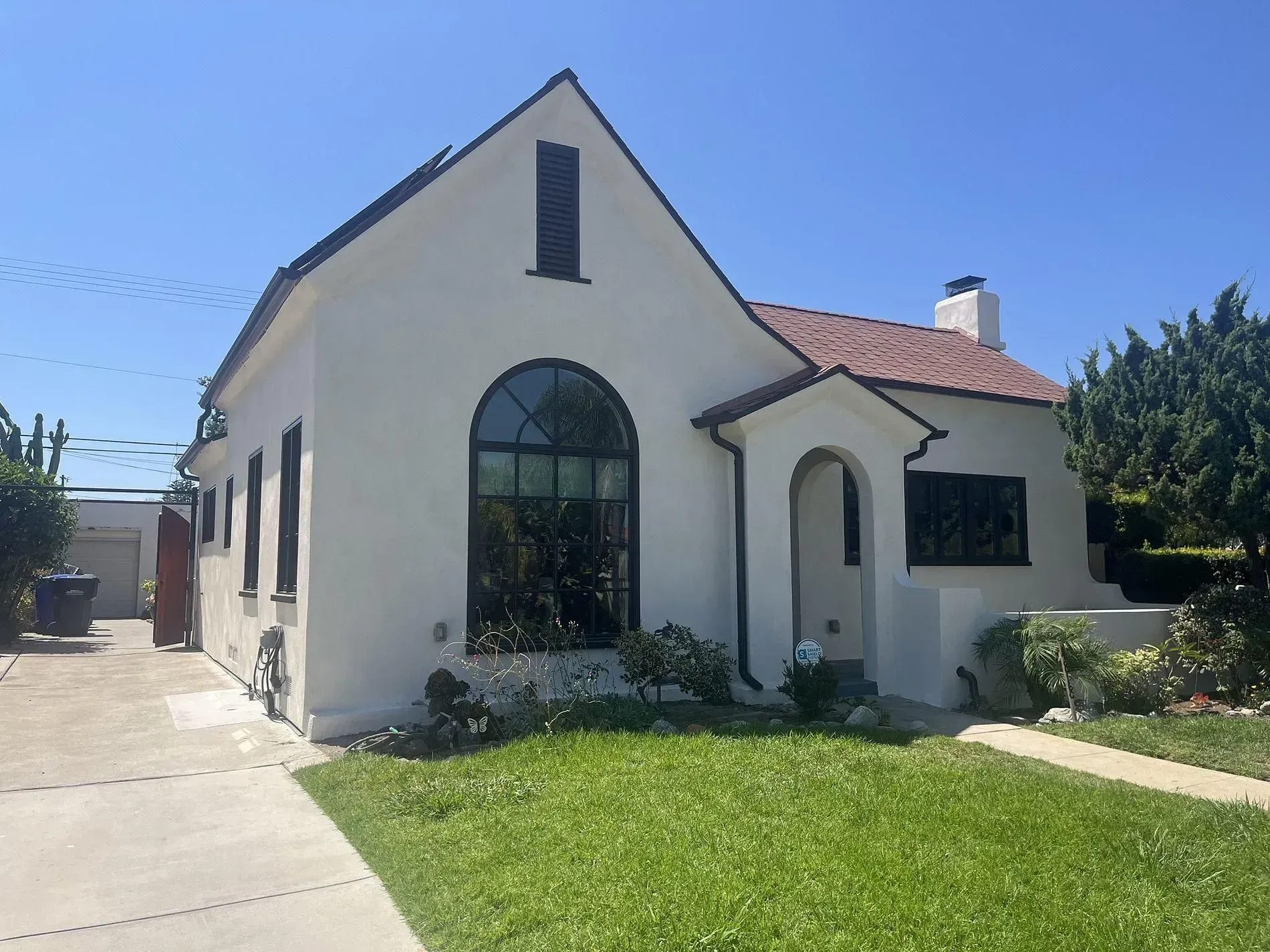 White stucco house with red tile roof, arch-top window and entry, and green lawn on a sunny day.