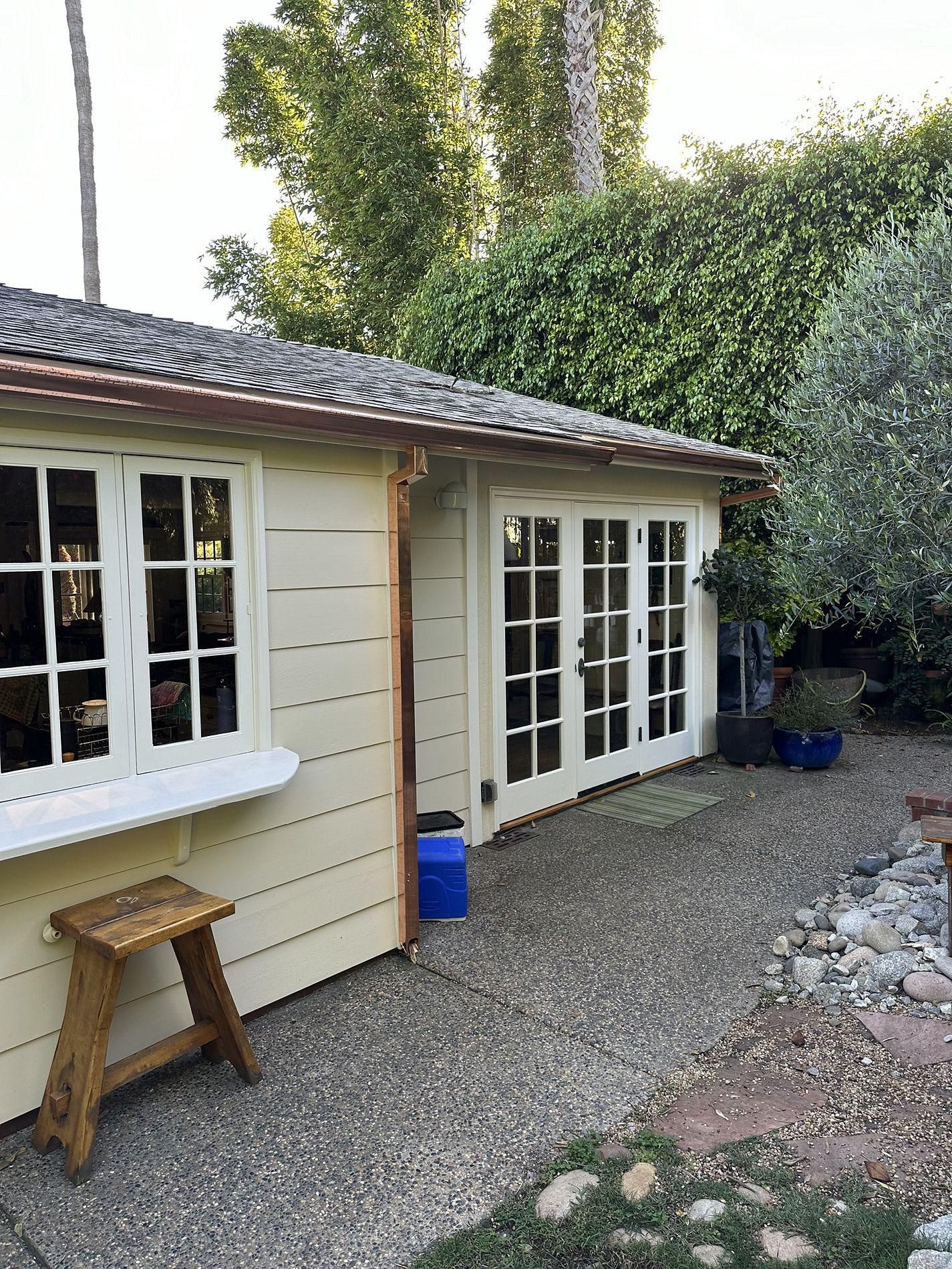 A white house with french doors and a wooden bench in front of it.