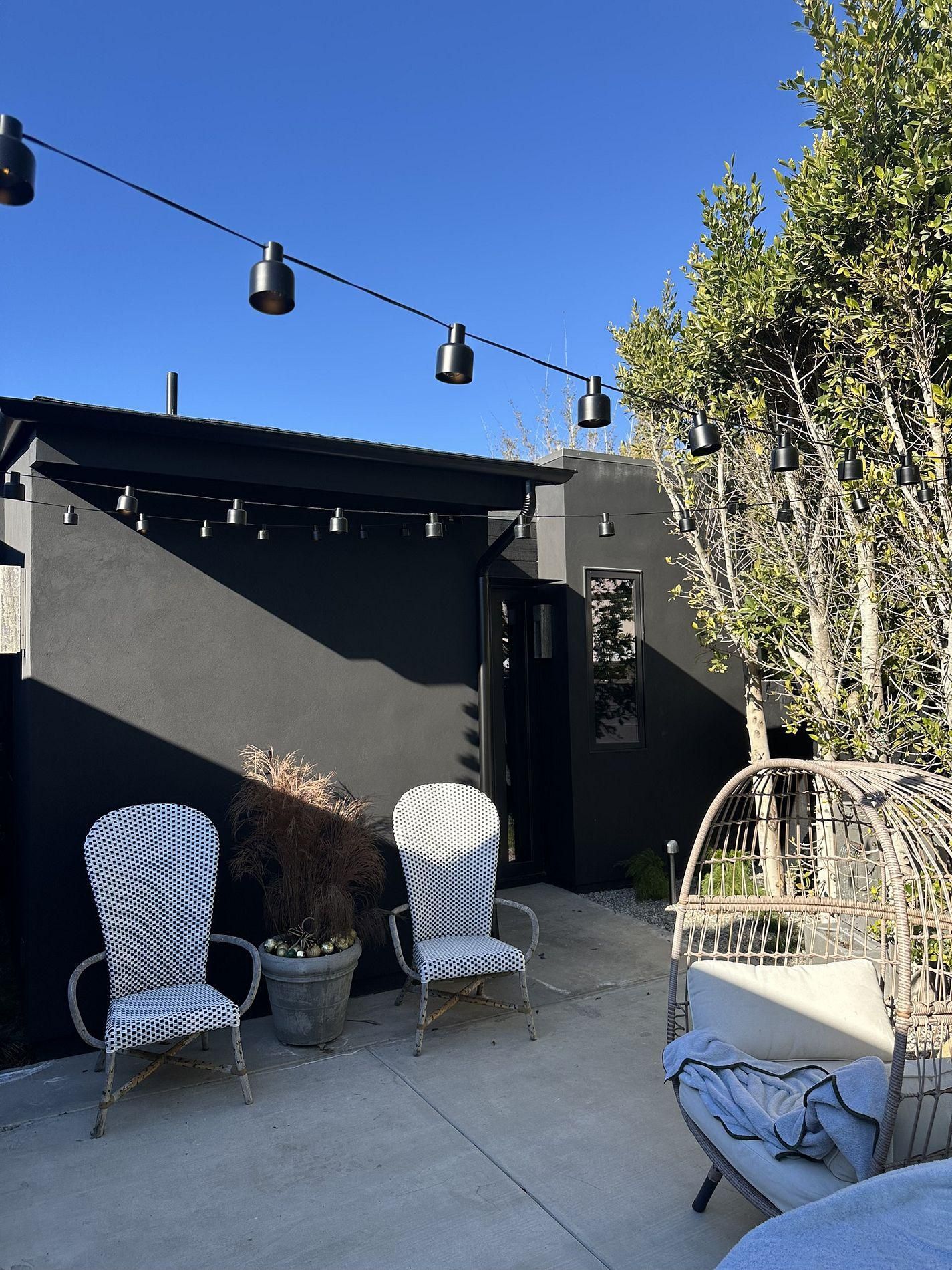 A patio with chairs, a table, and a string of lights hanging from the ceiling.