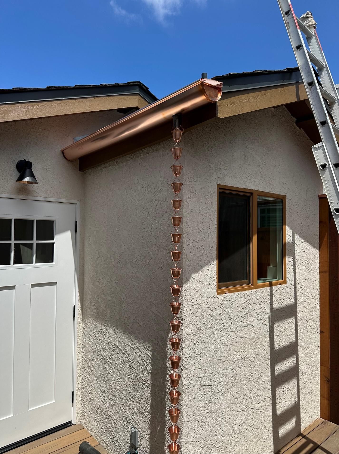 A copper rain chain is attached to the side of a house.