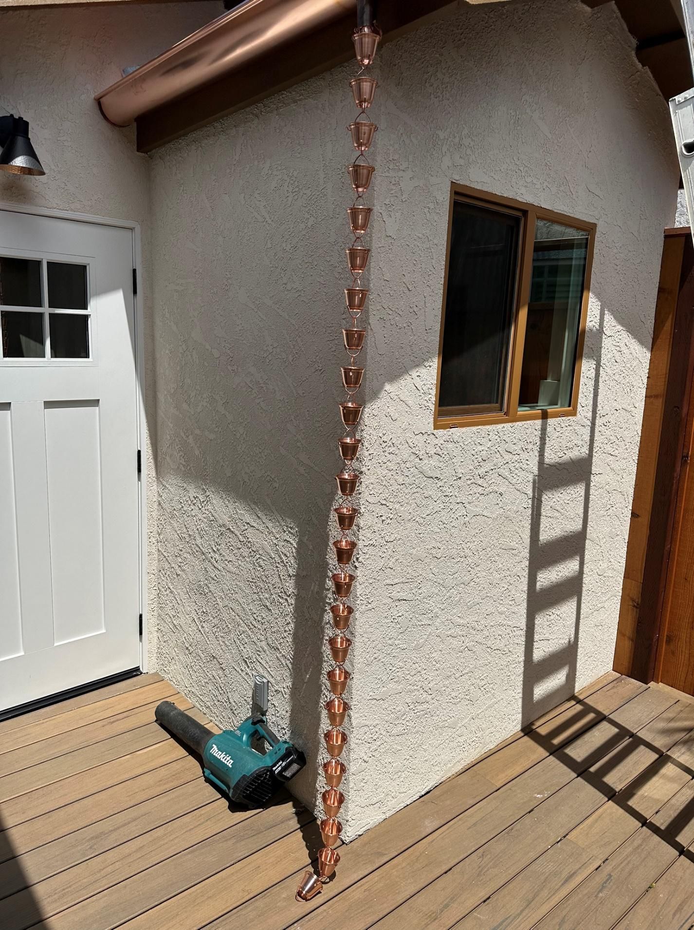 A copper rain chain is hanging from the side of a building.