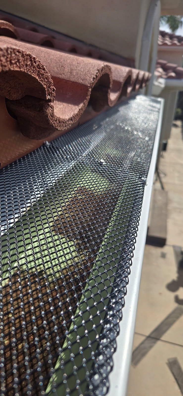 A close up of a gutter with a roof in the background.
