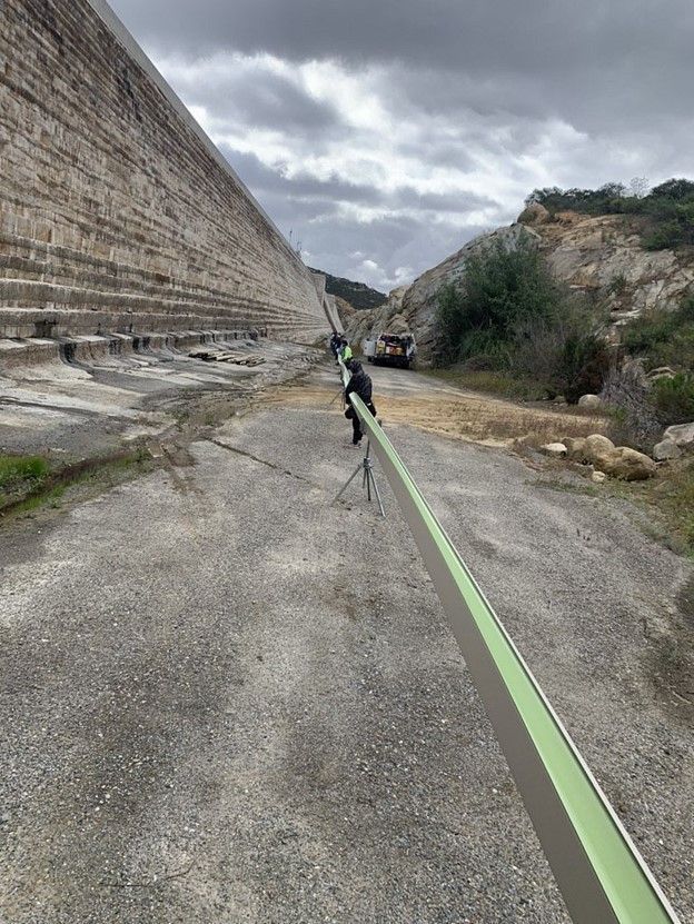 A person is walking a dog on a leash in front of a large stone wall.