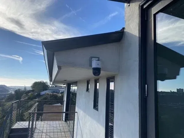 Security camera mounted on the exterior of a modern house with a view of a landscape and blue sky.