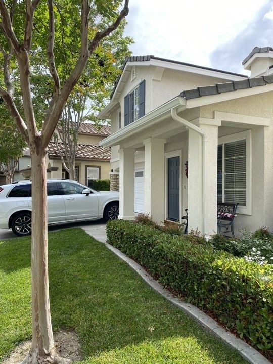 A white car is parked in front of a white house.