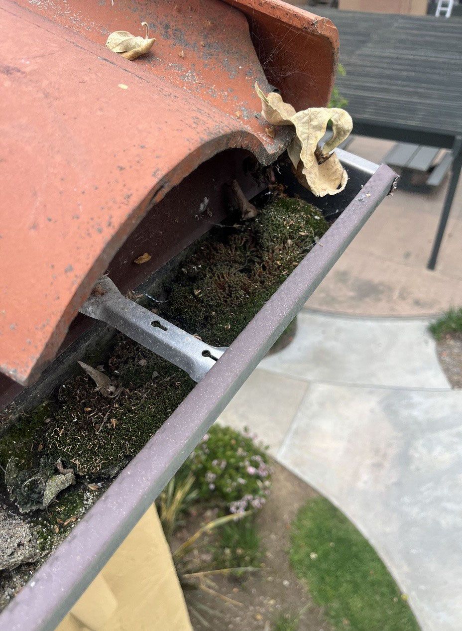A close up of a gutter with a tile roof in the background before