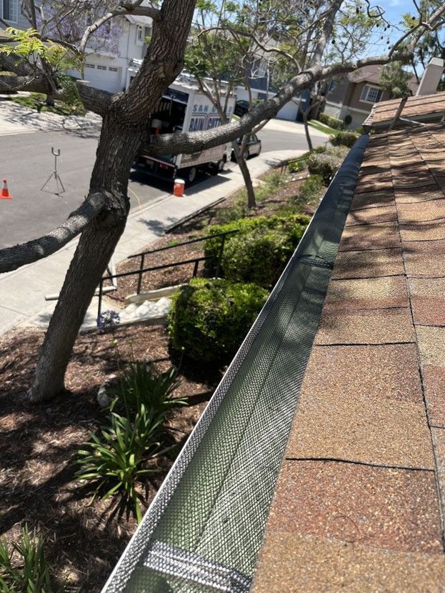 A gutter is being installed on a roof next to a tree.
