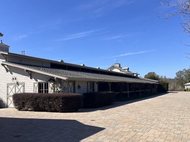 A large white barn with a brick driveway in front of it on a sunny day.