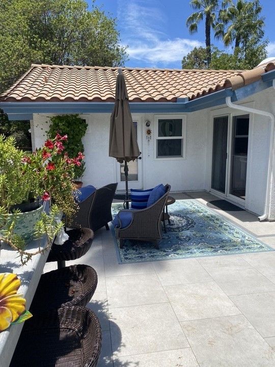 A patio with chairs and umbrellas in front of a white house.