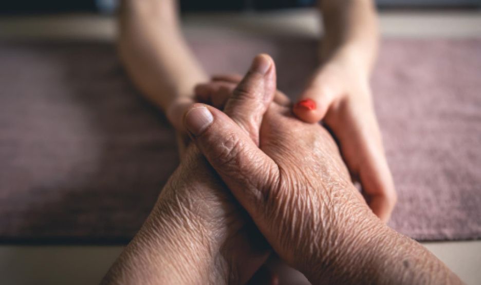 A woman is holding the hands of an older man.
