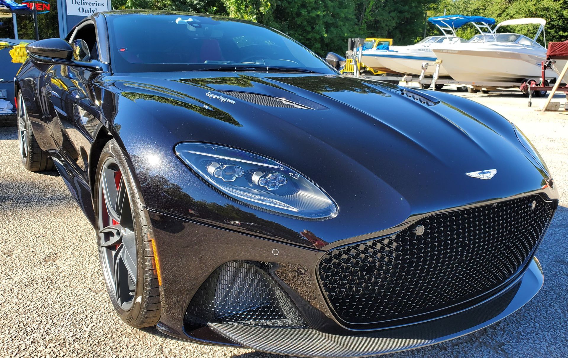 A black sports car is parked in a gravel lot next to a boat.