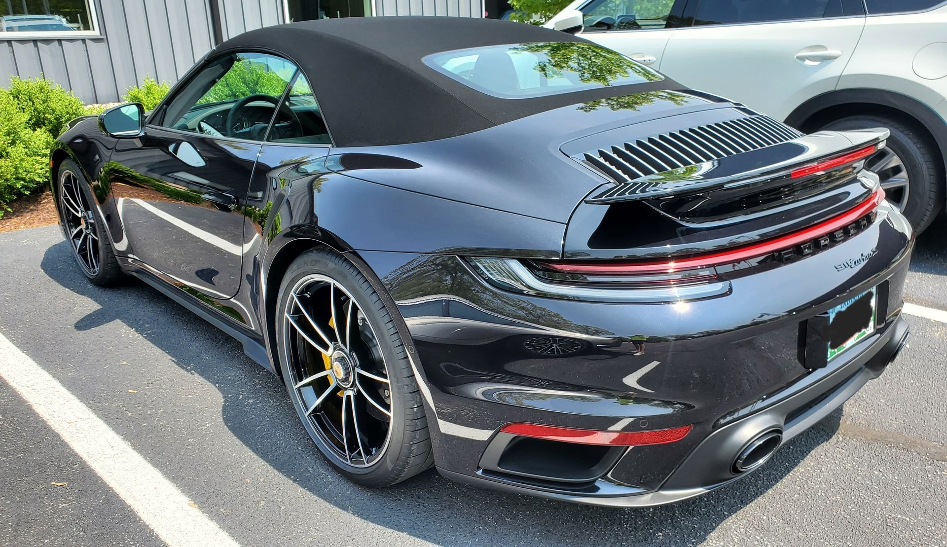 A black porsche 911 turbo s convertible is parked in a parking lot.
